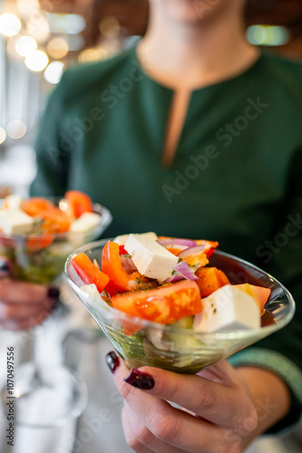 A close-up stock photo of a person in a green top holding two glass bowls of Greek salad with feta cheese and fresh vegetables. Perfect for healthy eating, culinary blogs, and food-related content.