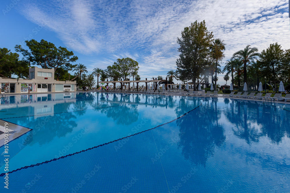 Magnificent view, swimming pool with blue sky with clouds. Holiday hotel in Antalya. Great relaxation and peaceful atmosphere, palm trees, sun loungers reflections.