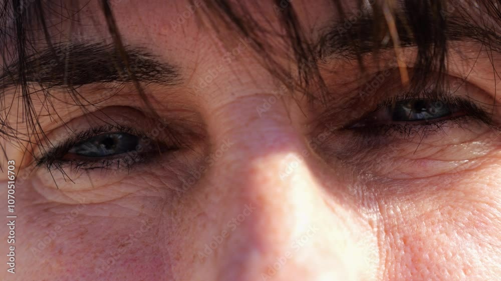 Tired blue eyes of a female blinking and looking into camera outdoor. Face of adult woman illuminating by bright rays of sun. Upset facial expression of lady. Close up Slow motion