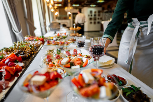 A close-up of a buffet table at a catered event, featuring an array of gourmet appetizers and a server pouring red wine into a glass. Perfect for illustrating catering services, event planning