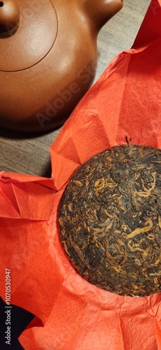 Pressed Chinese tea, black puer tea in the red cover. Small clay teapot on the wooden table  photo