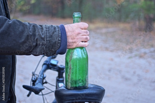 man holding big green empty glass bottle on black bicycle seat on autumn street