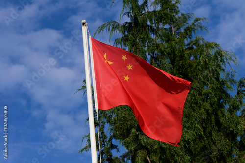 Waving Chinese flag against a backdrop of blue skies and lush greenery during a sunny day