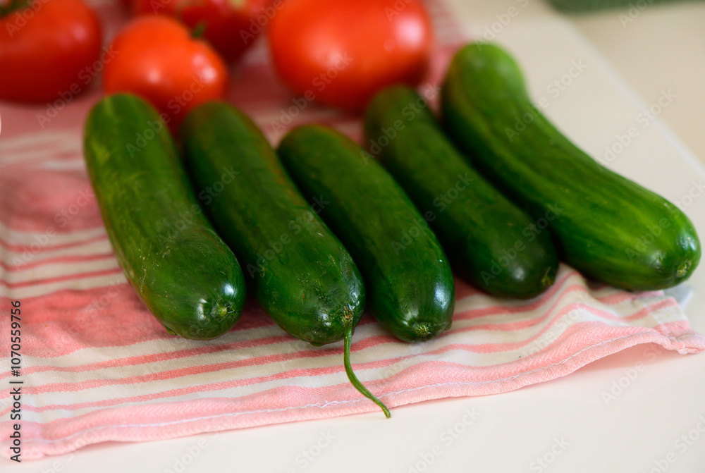 Fresh cucumbers and ripe tomatoes arranged artistically on a kitchen countertop during a sunny afternoon Fresh cucumbers and ripe tomatoes arranged artistically on a kitchen countertop during a sunny afternoon