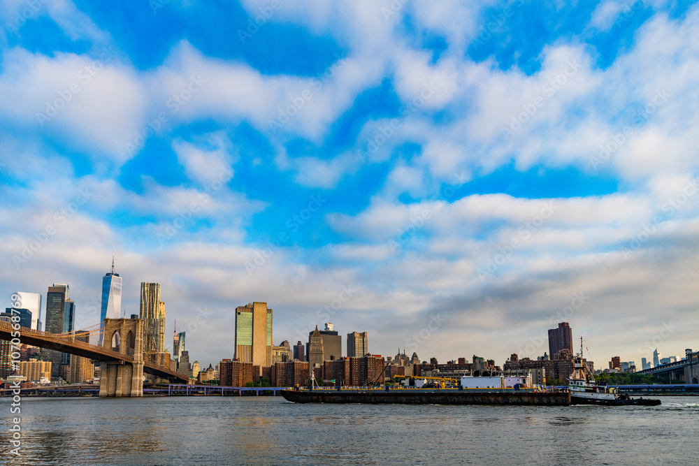 Naklejka premium Brooklyn bridge of New York city. Brooklyn landmark. Manhattan cityscape with skyscraper architecture. Brooklyn bridge to Manhattan. Urban architecture of New York city. Tugboat and barge