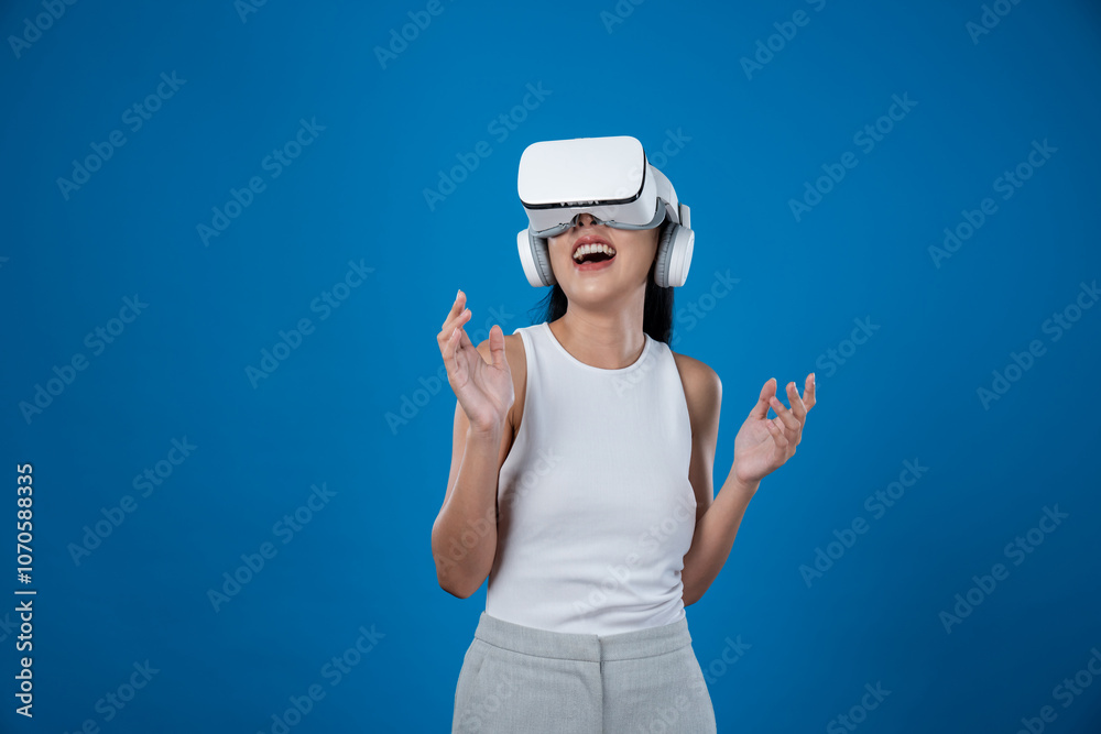 Smart female standing with blue background wearing VR headset connecting metaverse, futuristic cyberspace community technology. Elegant woman excited seeing generated virtual scenery. Hallucination. Smart female standing with blue background wearing VR headset connecting metaverse, futuristic cyberspace community technology. Elegant woman excited seeing generated virtual scenery. Hallucination.