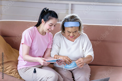 Obraz na płótnie Asian young woman teach older mother, how to wear face mask in living room with carefully. family concept w salonie
