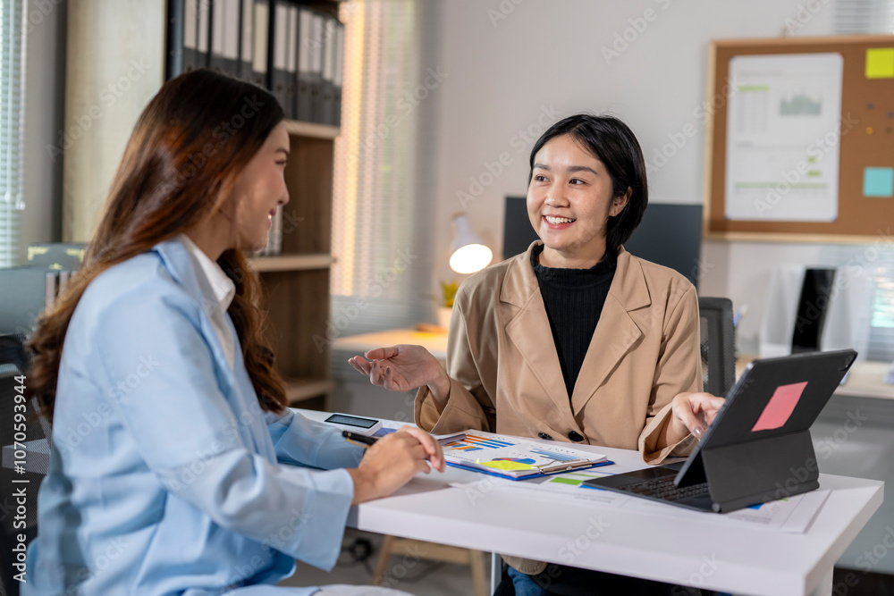 Two asian businesswomen are discussing new project ideas using a tablet and documents with financial charts at the office Two asian businesswomen are discussing new project ideas using a tablet and documents with financial charts at the office