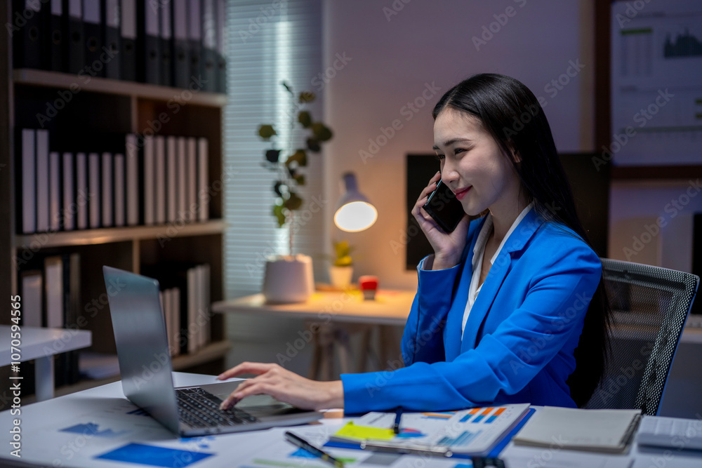 Businesswoman working late using laptop and talking on phone in office at night Businesswoman working late using laptop and talking on phone in office at night