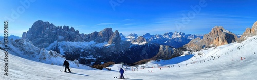 Skiers enjoy a sunny day on the slopes at Sella Nevea, surrounded by stunning snow-capped peaks and a vibrant blue sky photo