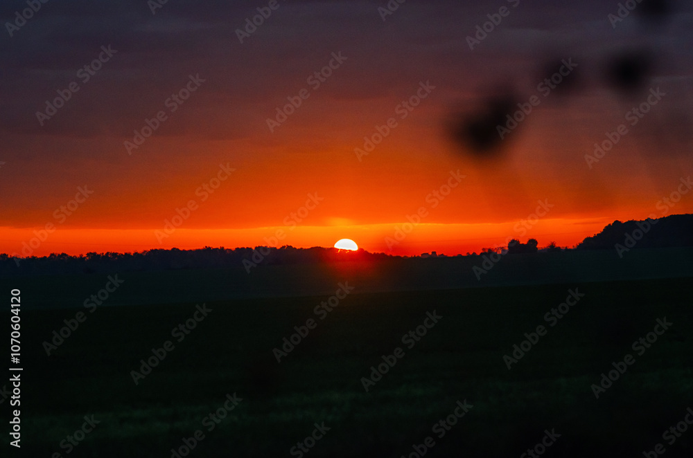 Magical orange and purple autumn sunset over a field with silhouetted trees on the horizon. Dusk. Magical orange and purple autumn sunset over a field with silhouetted trees on the horizon. Dusk.