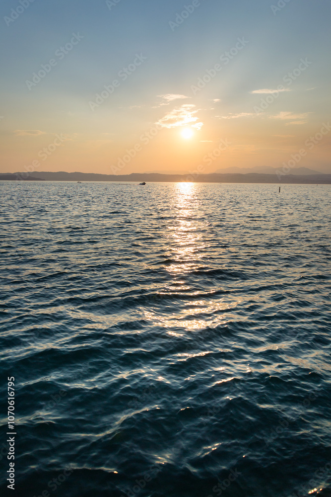 Fototapeta premium Beautiful purple sunset with floating boat on Lago di Garda near Scaliger Castle, Sirmione, Italy, romantic love concept