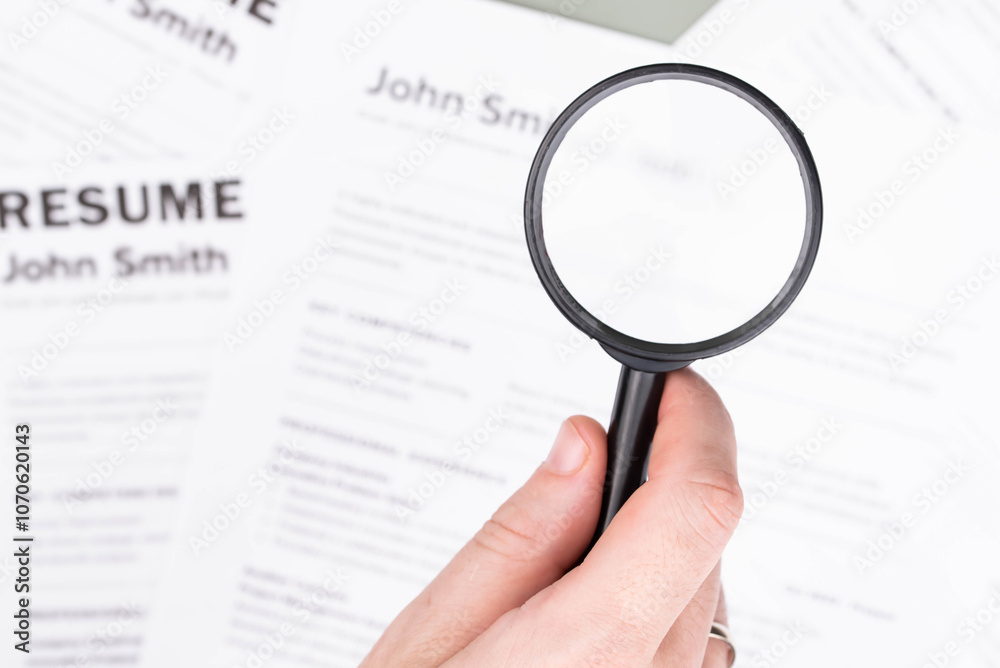 Mock CV (curriculum vitae) resume for John Smith, selected by HR under a magnifying glass, of careful review and assessment in the job recruitment process concept. Mock CV (curriculum vitae) resume for John Smith, selected by HR under a magnifying glass, of careful review and assessment in the job recruitment process concept.