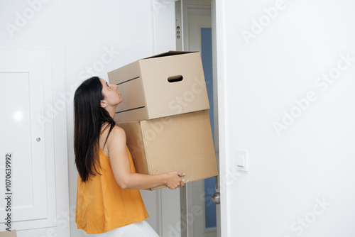 Young woman arriving home with moving boxes. She carries two heavy boxes and walks through the door. Real estate, mortgage, new life.