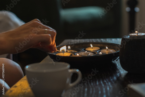 Wallpaper Mural atmospheric background for coziness and relaxation female hand lights candles. cups are on the table. in the background is a cozy chair Torontodigital.ca
