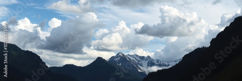 A majestic mountain range peeks through fluffy white clouds on a clear, blue day