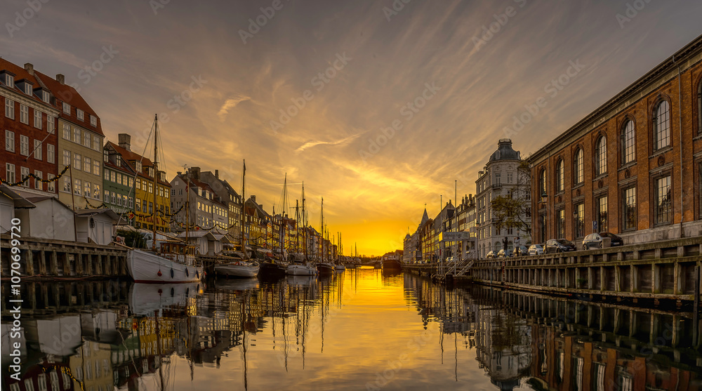 Sunrise over Nyhavn Canal in Copenhagen light and buildings reflect in the calm water
