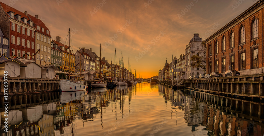 Sunrise over Nyhavn Canal in Copenhagen light and buildings reflect in the calm water