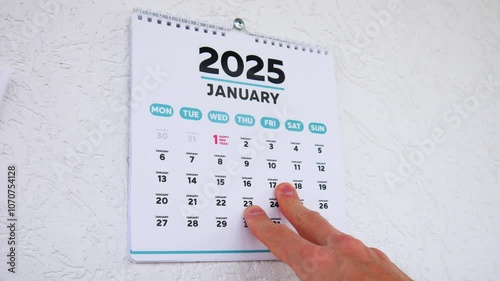 Close-up of male hands tearing off the title page of a wall calendar 2025 followed by the January month with the date of New Year photo