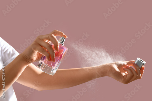 Young woman spraying elegant perfume on pink background, closeup