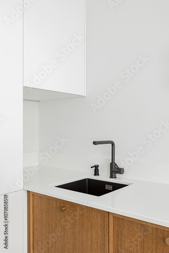 White kitchen table top, black sink with water tap, against a white wall