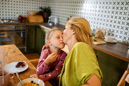 Mother kissing daughter during breakfast in cozy kitchen photo