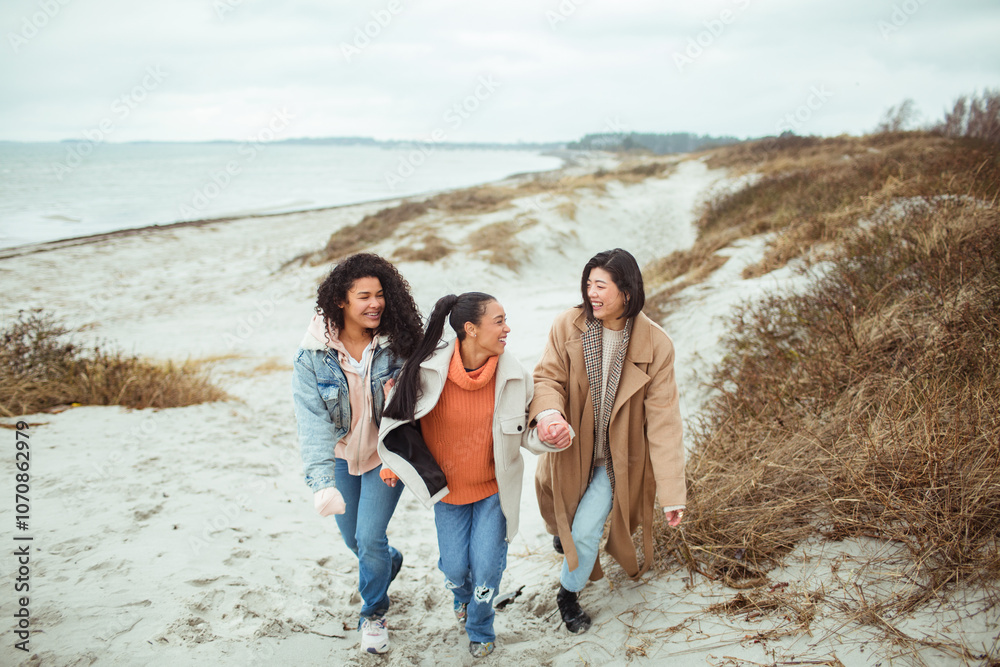 Three diverse female friends walking on a beach during winter Three diverse female friends walking on a beach during winter