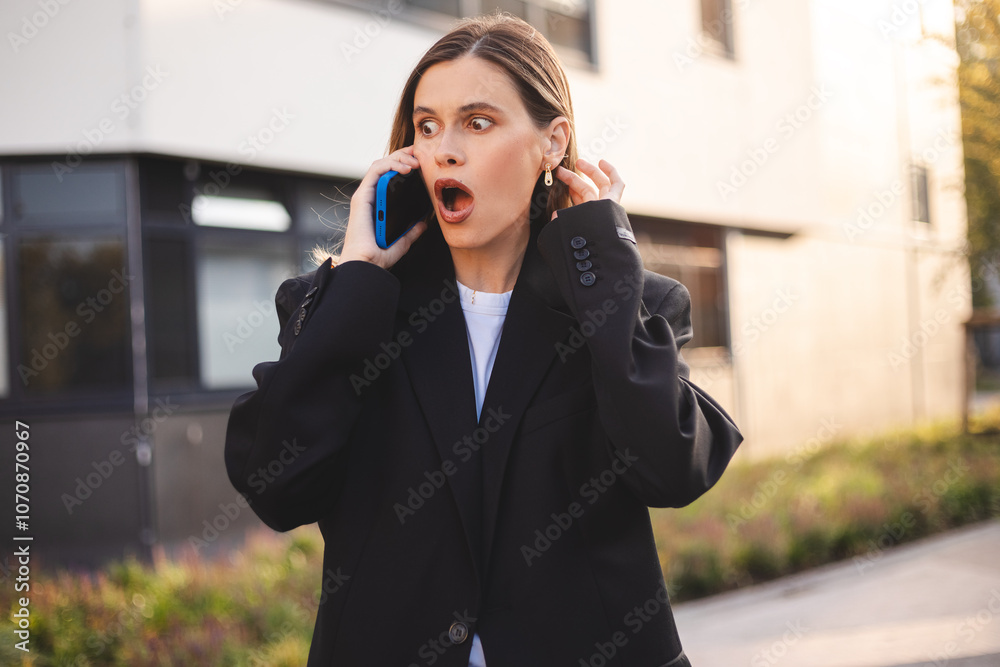 Shocked business woman having argument talking via smartphone. Angry young female speak irritated by cell phone, hear bad news using phone, she look mad and scared, open mouth standing near office. Shocked business woman having argument talking via smartphone. Angry young female speak irritated by cell phone, hear bad news using phone, she look mad and scared, open mouth standing near office.