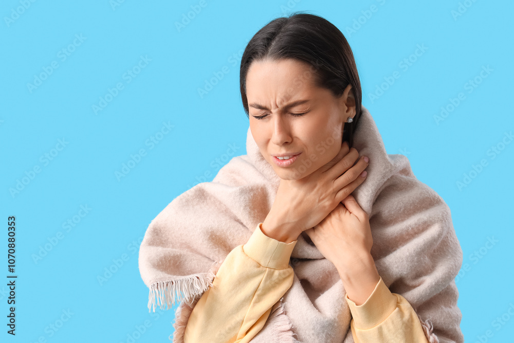 Young woman in scarf suffering from sore throat on blue background Young woman in scarf suffering from sore throat on blue background