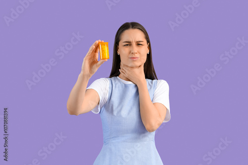 Young woman with pills for sore throat on lilac background