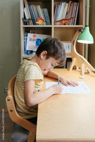 Focused caucasian schoolboy diligently doing his homework at his bedroom desk, with books and toys in the background