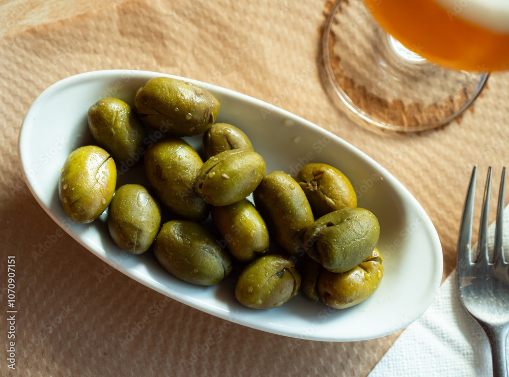 Bowl of green pickled olives with stone. On table there is ceramic bowl with vegetable snack for beer, wine Bowl of green pickled olives with stone. On table there is ceramic bowl with vegetable snack for beer, wine