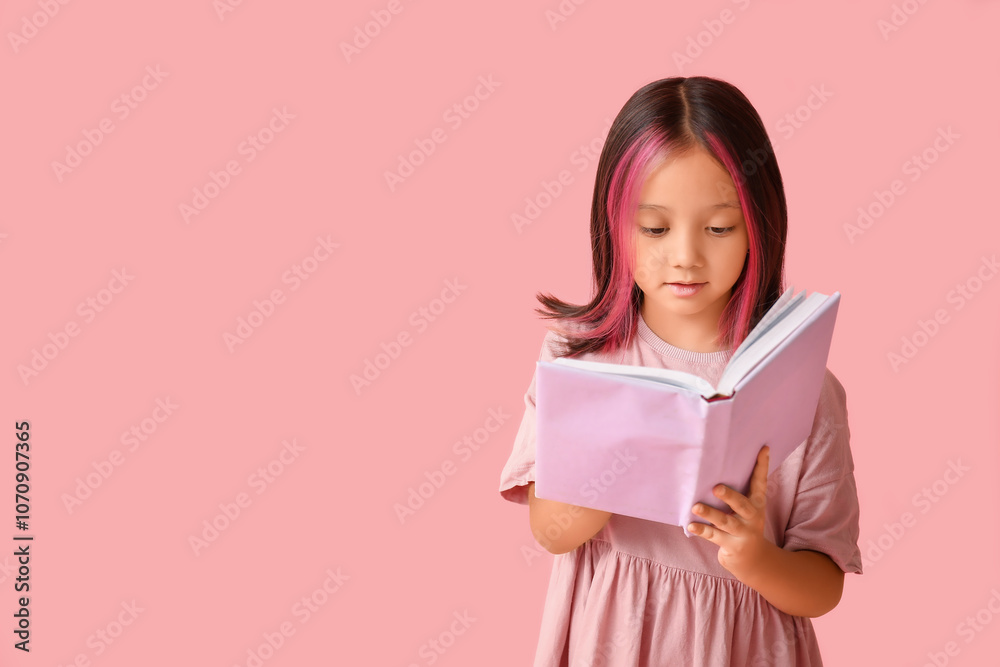Cute little Asian girl reading book on pink background Cute little Asian girl reading book on pink background