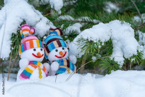 Snowman and snowwoman in christmas clothes stand under pine branch tree with white snow in winter forest. Knitted bauble. Christmas and new year holidays decoration. Symbol xmas of winter season. photo