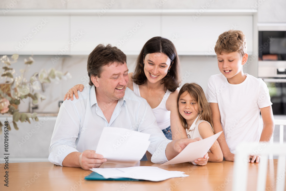 Happy father looking through papers sitting in the kitchen together with wife and children Happy father looking through papers sitting in the kitchen together with wife and children