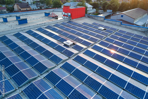 Aerial view of solar power plant with blue photovoltaic panels mounted on industrial building roof for producing green ecological electricity. Production of sustainable energy concept