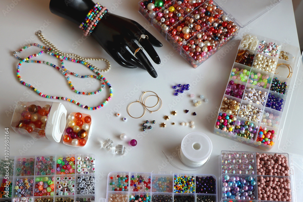 Obraz premium Hand figurine, colorful friendship bracelets, necklaces, various beads and DIY supplies on the table. Making jewelry at home. Selective focus.