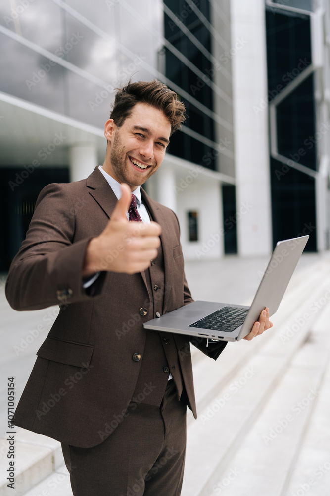 Vertical portrait of friendly businessman in urban setting, holding laptop and showing thumbs up gesture, smiling looking at camera, embracing confidence and professionalism in corporate world. Vertical portrait of friendly businessman in urban setting, holding laptop and showing thumbs up gesture, smiling looking at camera, embracing confidence and professionalism in corporate world.