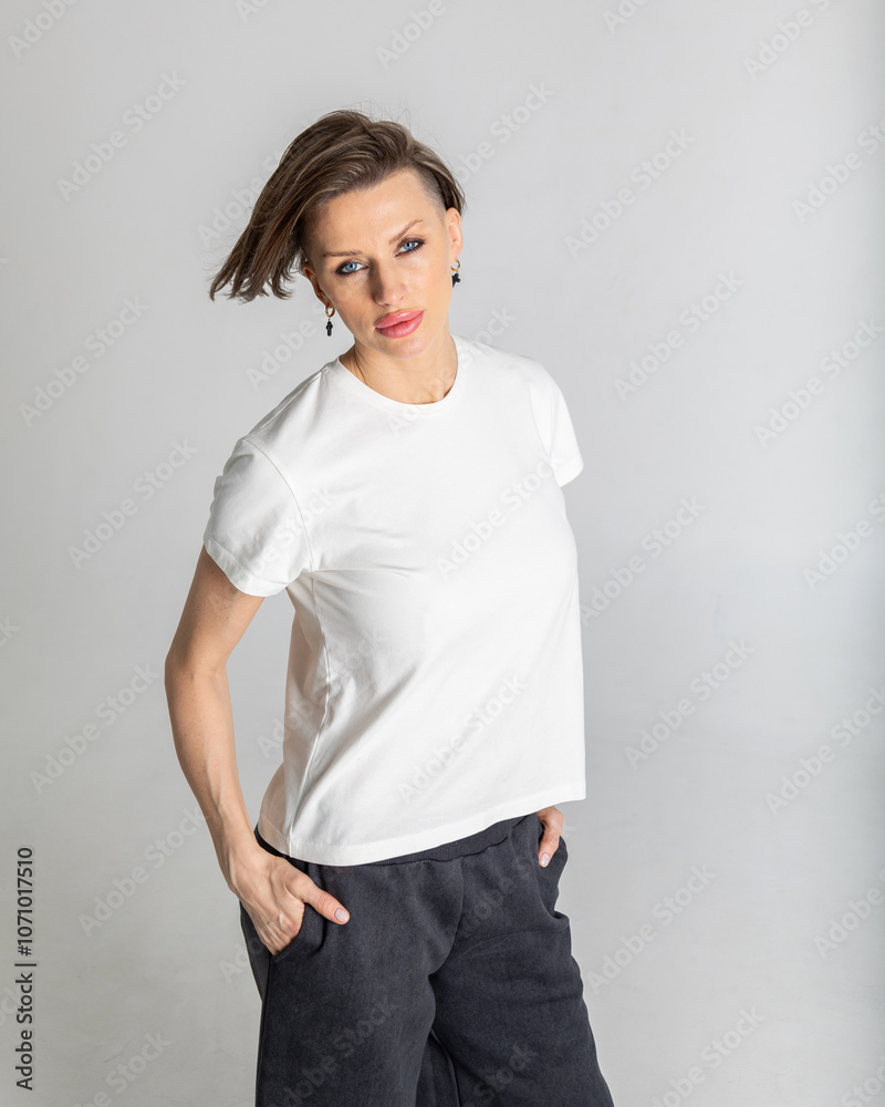 Portrait beautiful woman of model appearance. Girl in white T-shirt, black trousers on grey background. Pretty female with trendy makeup posing in studio. Vertical photo. Portrait beautiful woman of model appearance. Girl in white T-shirt, black trousers on grey background. Pretty female with trendy makeup posing in studio. Vertical photo.