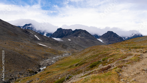 Nordic rocky nature with mountain glacier valley of Tarfala with breathtaking scenic view towards misty mountains and snow and highland grassy nature of swedish Lapland landscape.