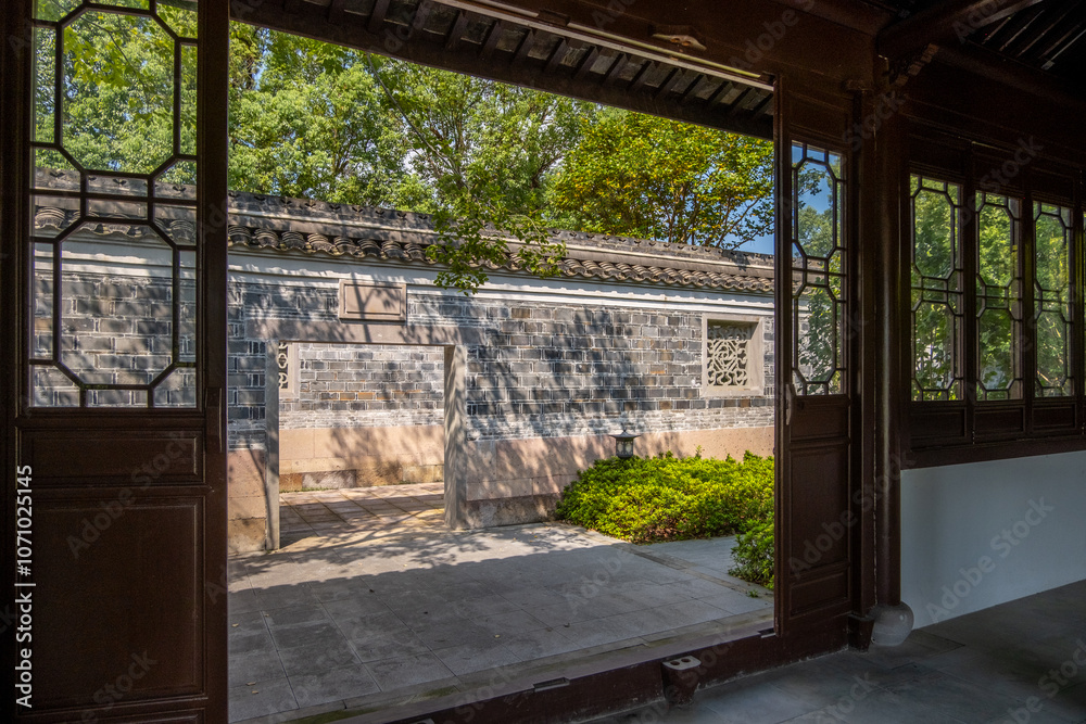 a traditional Chinese garden scene viewed from inside an old pavilion with intricate wooden lattice. A courtyard with a pathway leading to a brick wall, adorned with ornamental stone windows a traditional Chinese garden scene viewed from inside an old pavilion with intricate wooden lattice. A courtyard with a pathway leading to a brick wall, adorned with ornamental stone windows