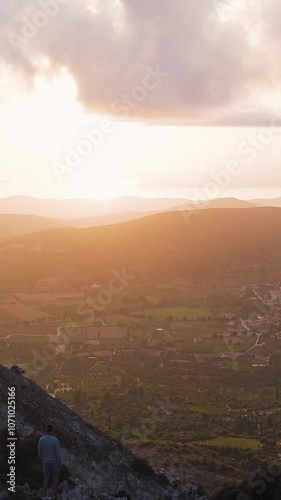 Man walks along a mountain ridge during golden hour, enjoying the scenic view of a valley below