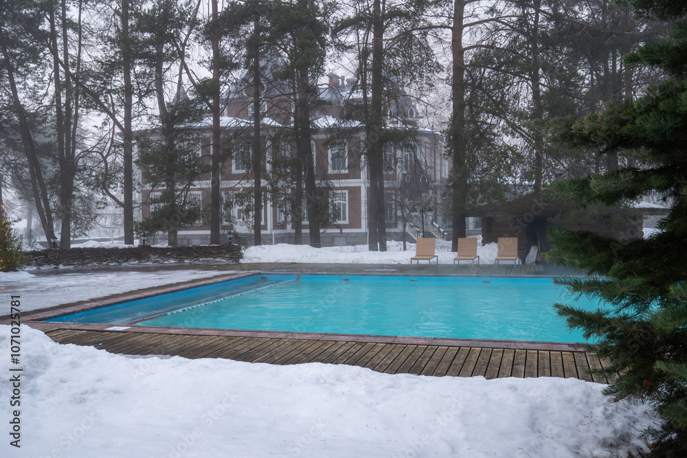 Outdoor swimming pool with warm water. Winter wellness spa resort with hot outdoor swimming pool with thermal water, foggy weather Outdoor swimming pool with warm water. Winter wellness spa resort with hot outdoor swimming pool with thermal water, foggy weather