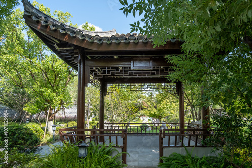 A traditional Chinese garden pavilion or gazebo with ornate wooden lattice work , wooden railings and curved tiled roof surrounded by plants and trees.The peaceful resting spot in a park in China. photo