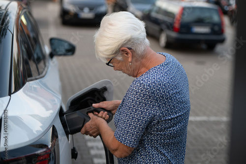 Elderly Woman Attaching Charging Cable to Electric Vehicle in Parking Lot