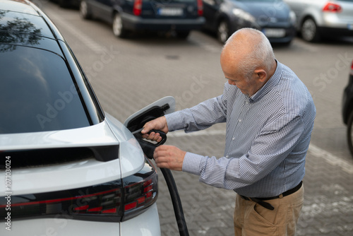 Senior Man Attaching Charging Cable to Electric Car in Parking Lot