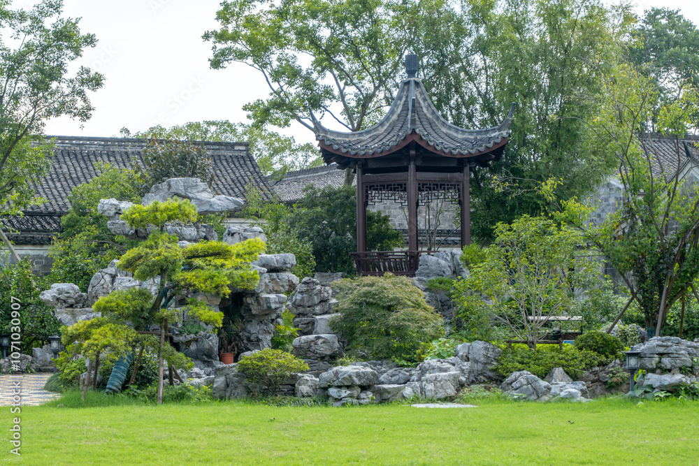 Obraz premium A tradtional Chinese garden featuring ornate rockery, pavilion or gazebo with curved roofline, and lush greenery, stone formations, manicured lawn, and classical architecture.