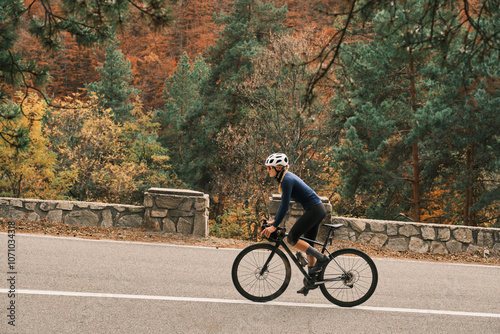 Woman cyclist rides road bike through scenic autumn landscape. Vibrant fall foliage provides stunning backdrop. Active lifestyle and outdoor adventure. Romania. Carpathian Mountains. Transylvania