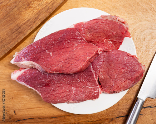 Raw beef veal meat tenderloin lie next to spices - process of cooking homemade festive dish. There is veal raw steak on table, meat processing before frying.