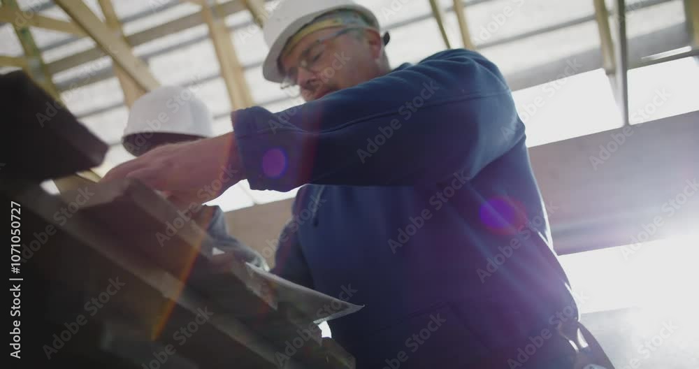 Construction supervisor gesturing and pointing while reviewing building plans with coworker on site, teamwork and guidance in structural project, safety helmets on